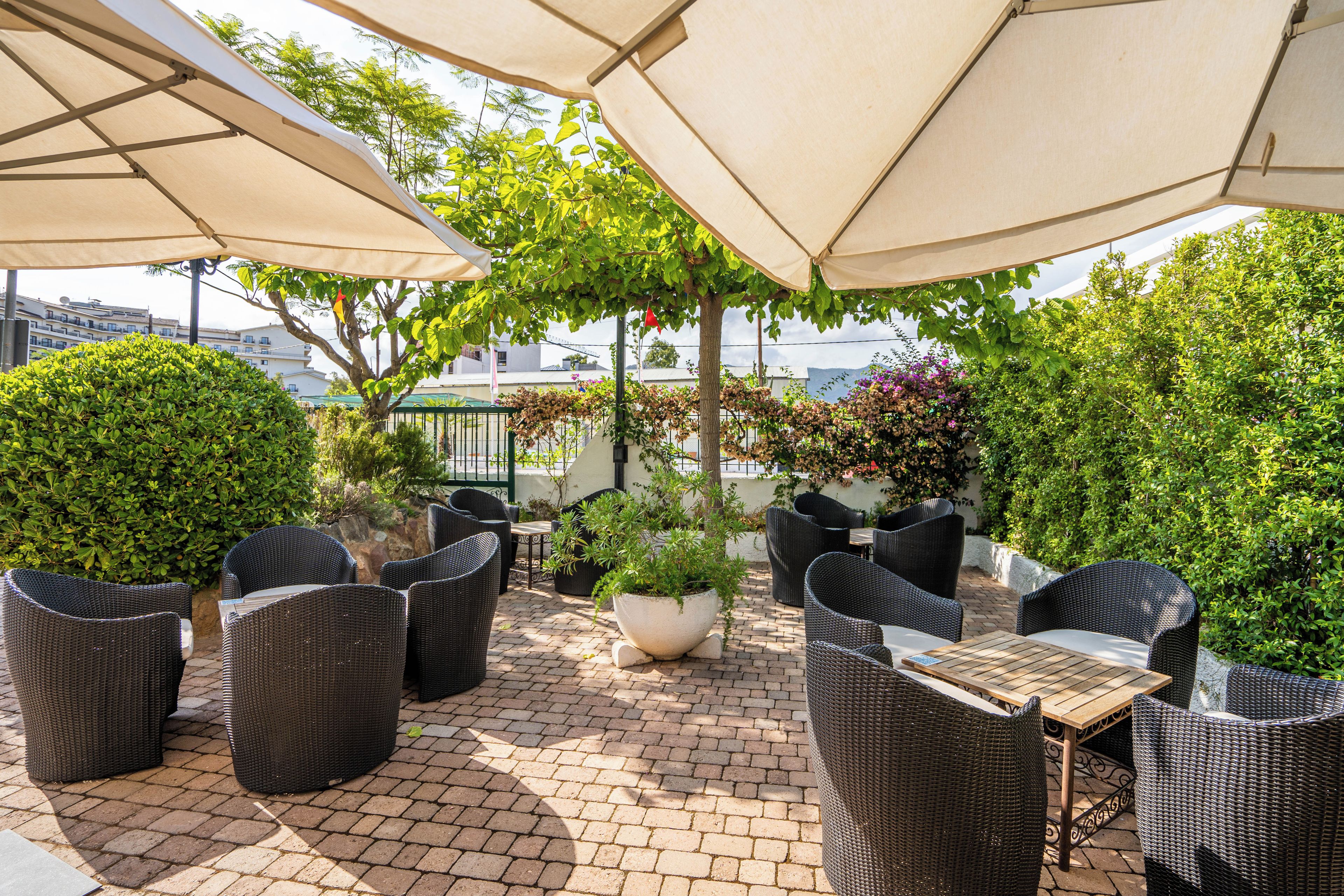 An outdoor patio with wicker furniture, umbrellas, and potted plants.