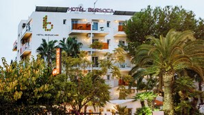 Un hôtel à plusieurs étages, doté de balcons, de palmiers et d’une enseigne indiquant qu’il s’agit d’un hôtel.