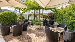 Une terrasse extérieure aménagée avec des meubles en osier, des parasols et des plantes en pot.