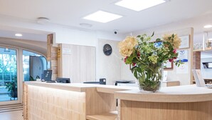 Un comptoir d’accueil orné d’un vase de fleurs, une horloge au mur et une vue sur l’extérieur.