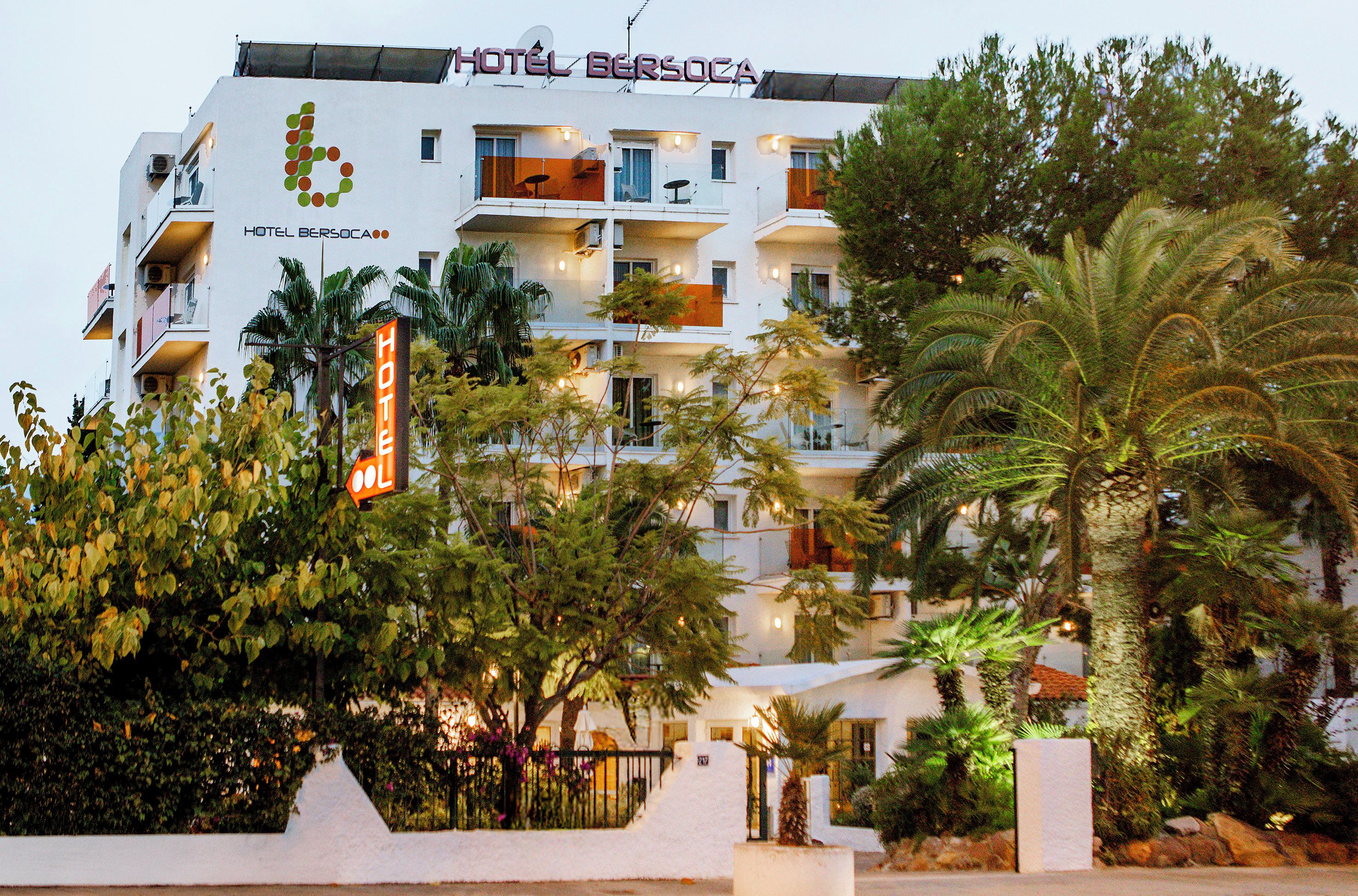 Un hotel de varios pisos con balcones, palmeras y un letrero que indica que es un hotel.