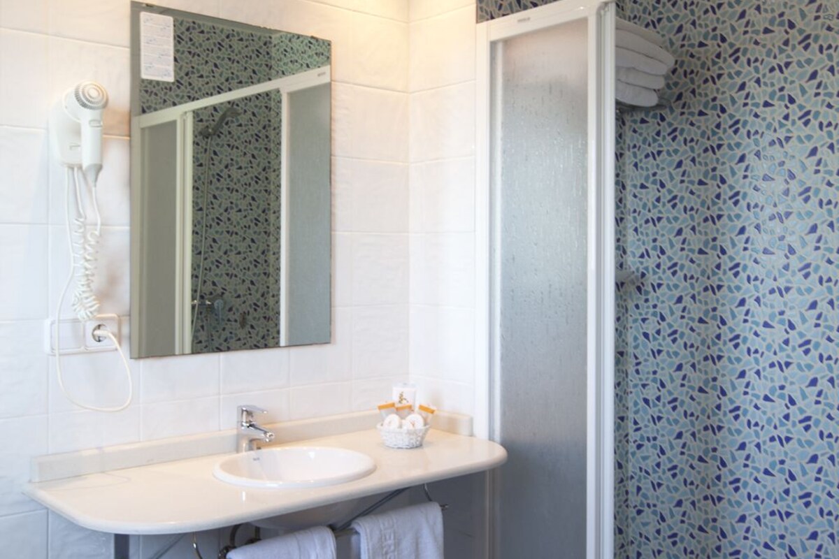 A bathroom with a white sink, a mirror, a hairdryer, and a shower with mosaic tiles.