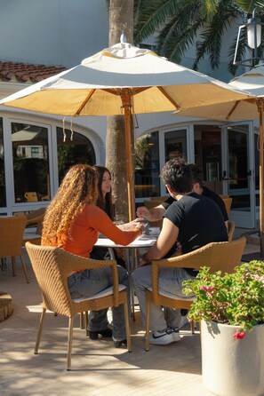 Un área de comedor al aire libre con sillas de mimbre y una mesa bajo un paraguas grande.