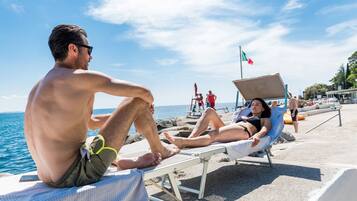Eine Strandansicht mit einem Mann und einer Frau, die am Wasser in Liegestühlen entspannen.