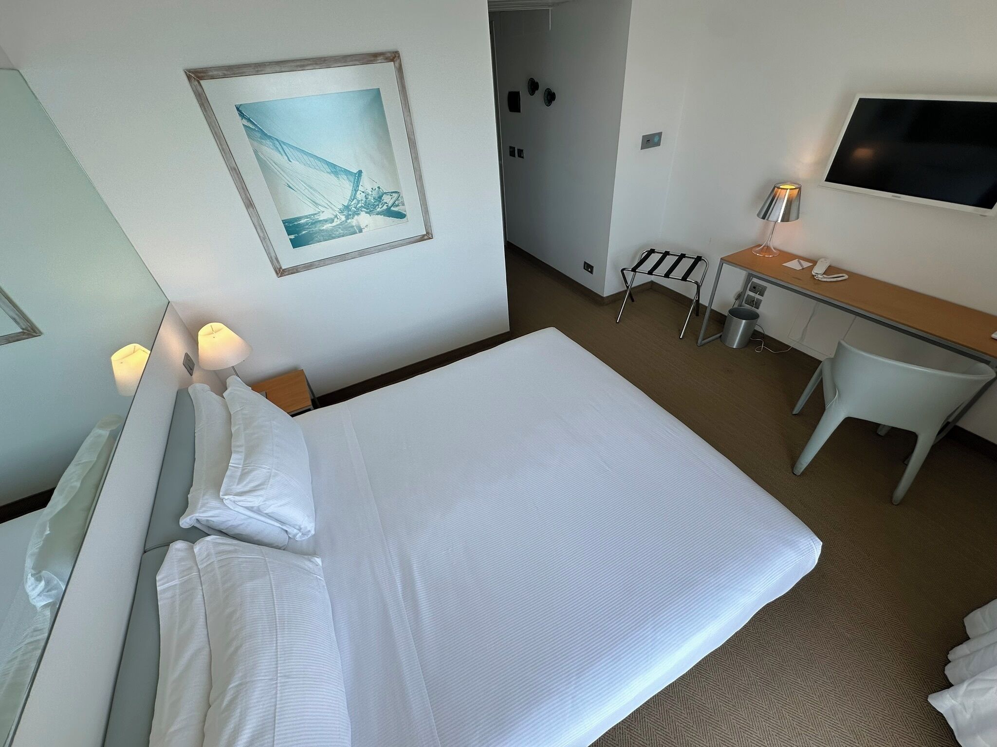 Habitación de hotel con una cama grande, un escritorio, una silla, un televisor y un cuadro en la pared.