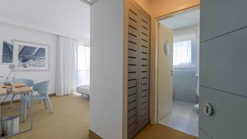 A modern hotel room with a desk, chairs, a wardrobe, and a bathroom visible through an open door.