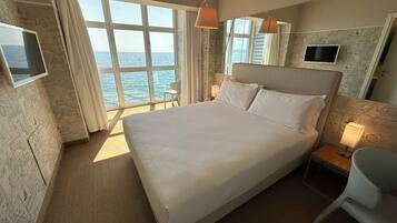 Ein Hotelzimmer mit einem großen Bett, einem Fernseher, einem Sessel und Blick aufs Meer.