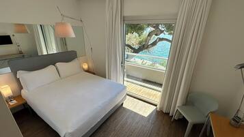 Habitación de hotel moderna con una cama grande, lámparas de noche, un televisor de pantalla plana y vista a una piscina y árboles.