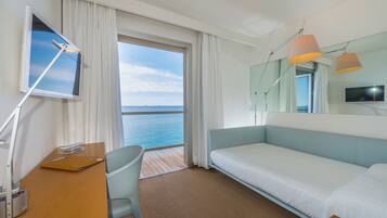 Habitació d'hotel amb un llit, una taula de treball, una cadira, un televisor i vistes al mar.