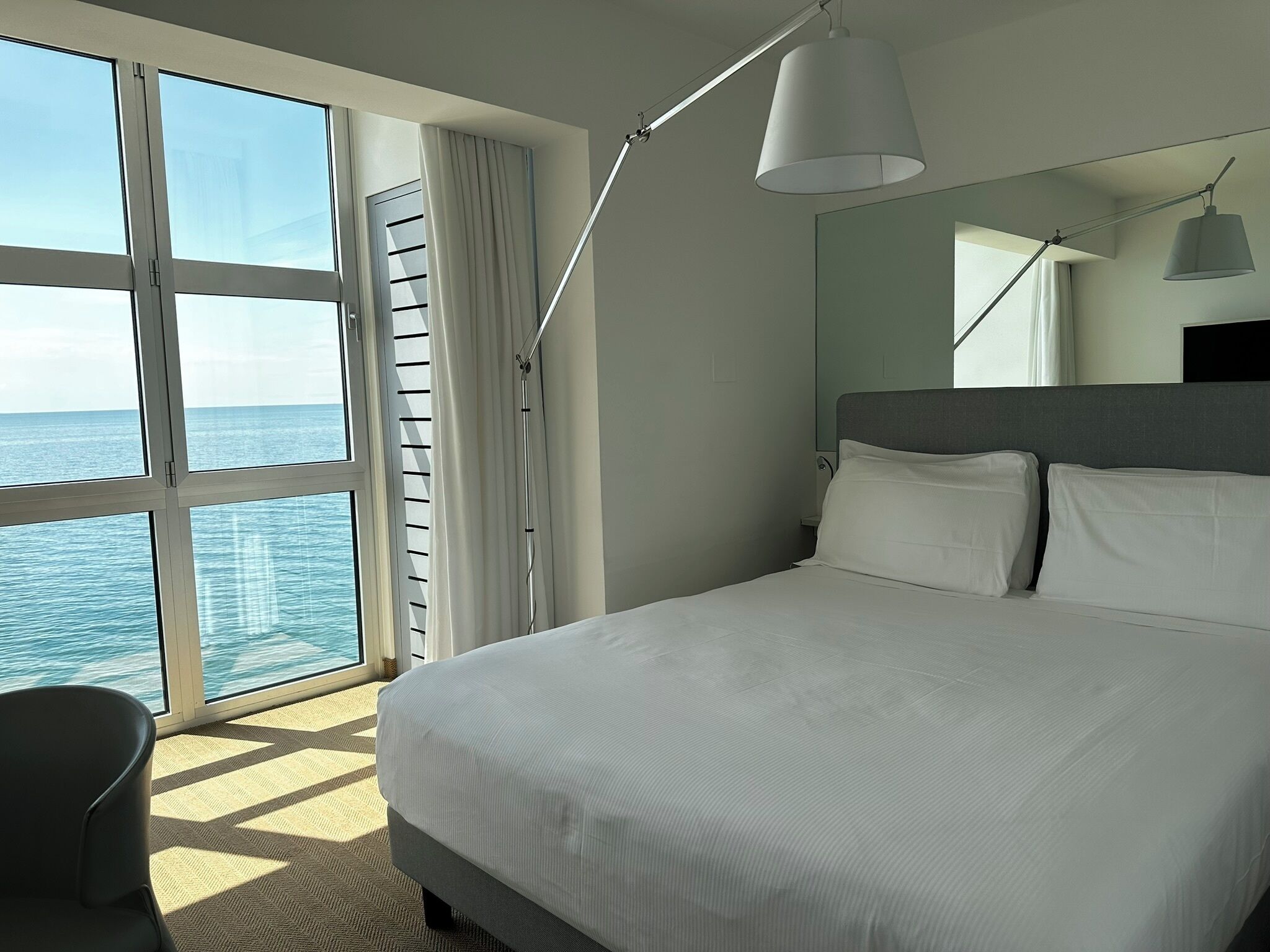 Une chambre d’hôtel avec un grand lit, une vue sur la mer et une lampe moderne.