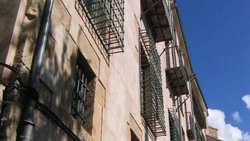 Un edificio con varias ventanas y balcones, que presenta fachada de piedra y un cielo azul despejado al fondo.