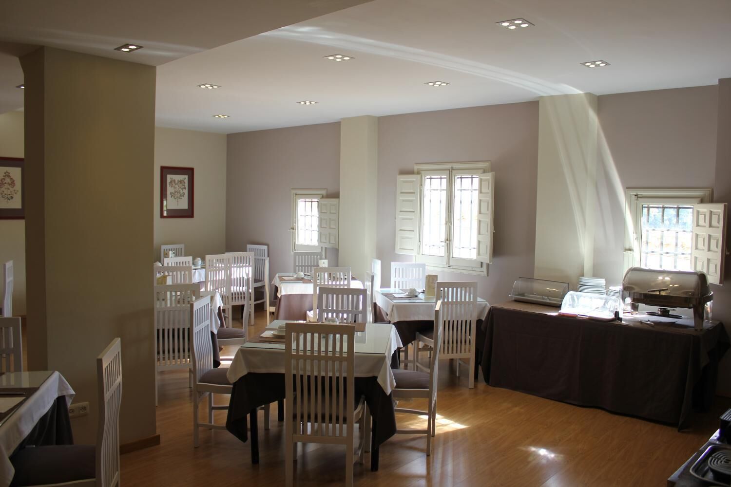 Un comedor con varias mesas y sillas, una estación de bufé y amplios ventanales que dejan entrar luz natural.