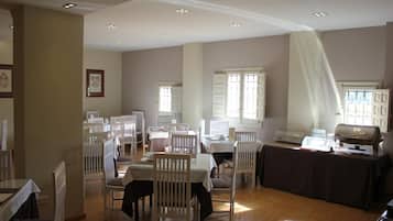 Un comedor con varias mesas y sillas, una estación de bufé y amplios ventanales que dejan entrar luz natural.