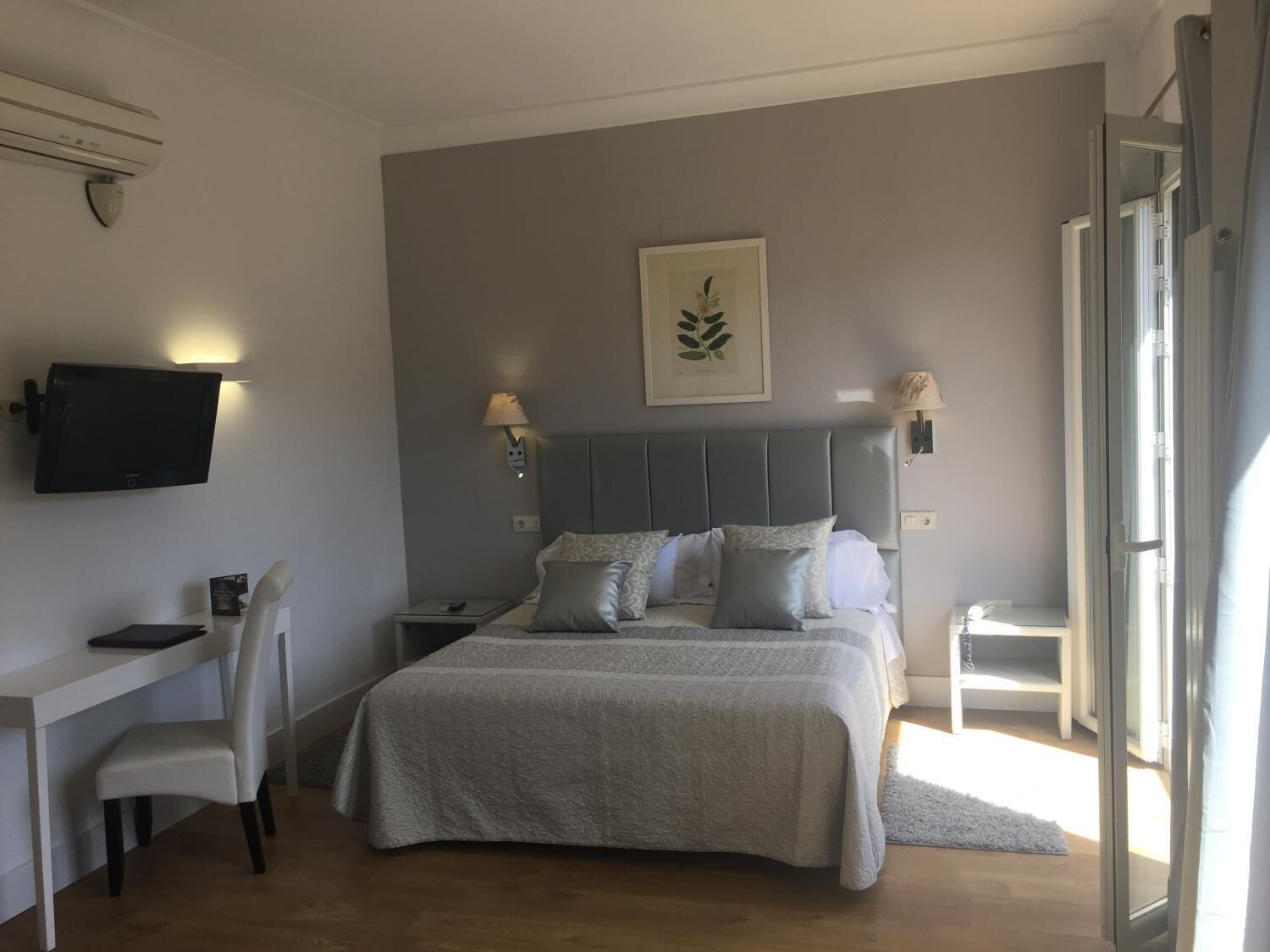 Ett sovrum med en säng, sänglampor, en väggmonterad tv, ett skrivbord med en stol och ett fönster.