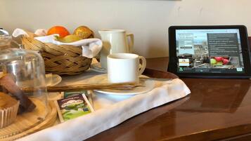 Un plateau de petit-déjeuner avec un panier de fruits, une tasse blanche, un pichet en verre et une tablette affichant un site web.