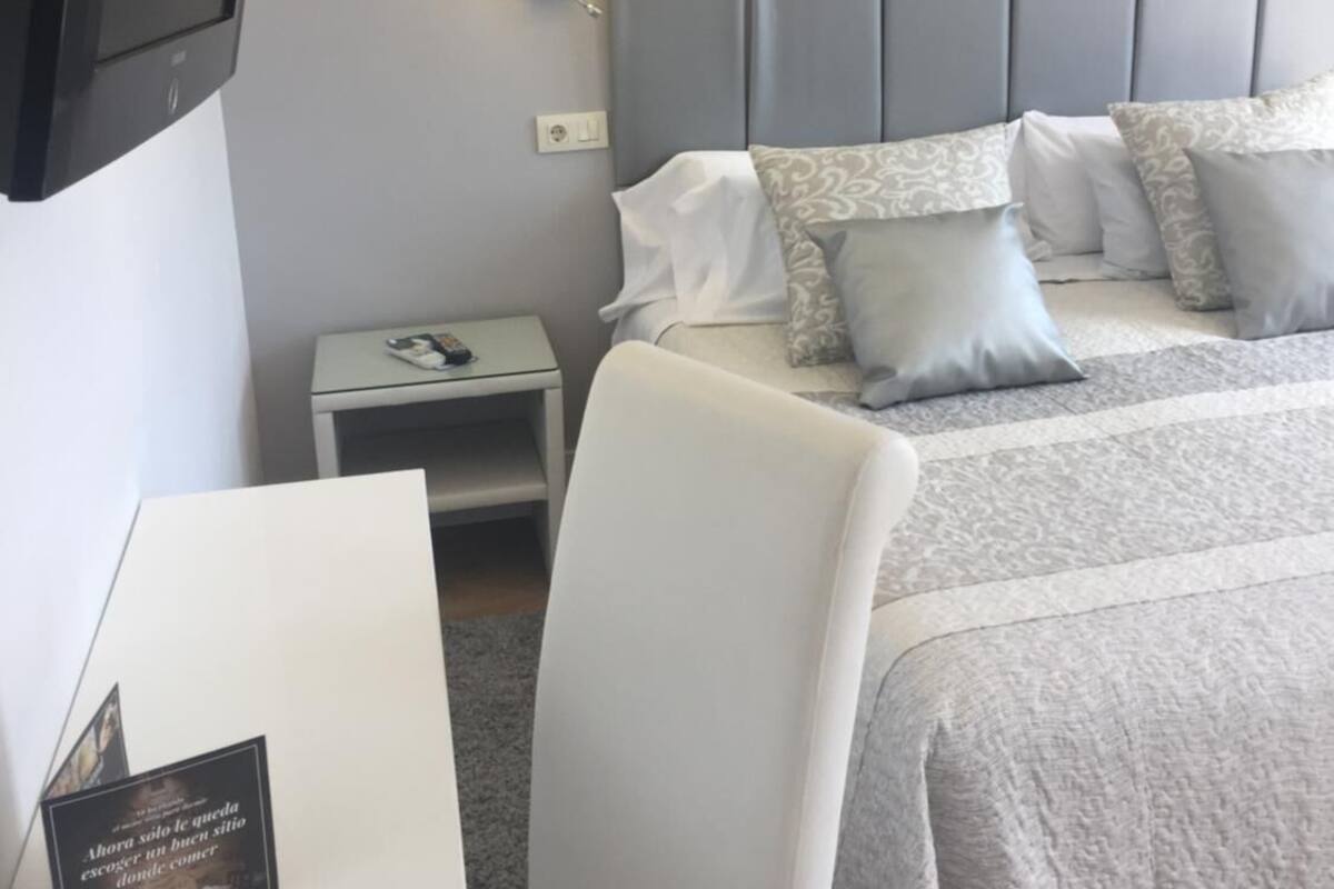 Habitación de hotel con cama, mesita de noche, televisor e impresión enmarcadas de motivos botánicos en la pared.