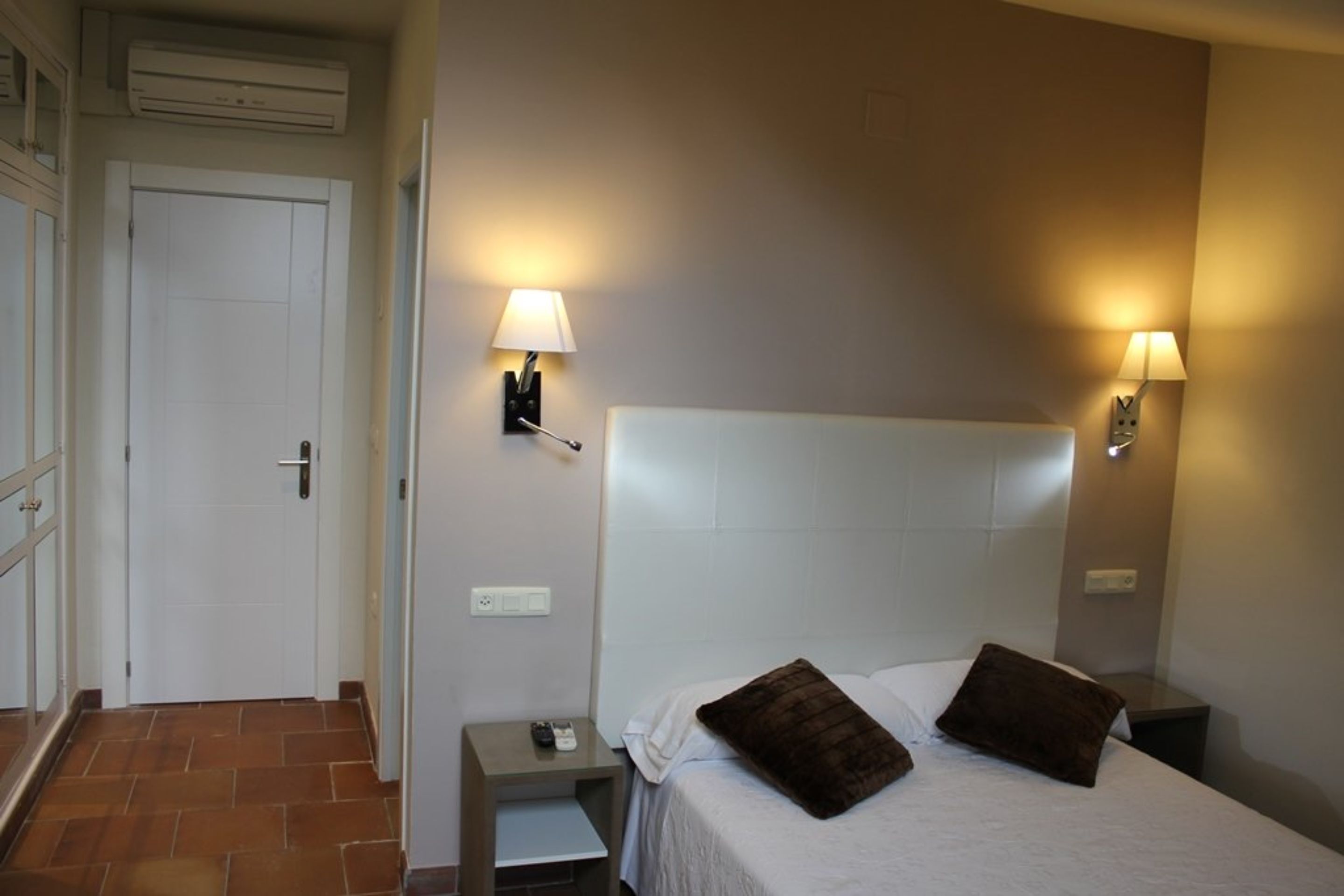 Una habitación de hotel con una cama, dos mesitas de noche, una lámpara y una puerta.