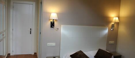 Una habitación de hotel con una cama, dos mesitas de noche, una lámpara y una puerta.