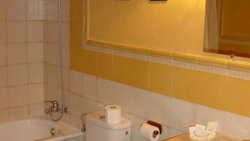 Un baño con bañera, inodoro, lavamanos y dos lámparas fijadas a la pared.