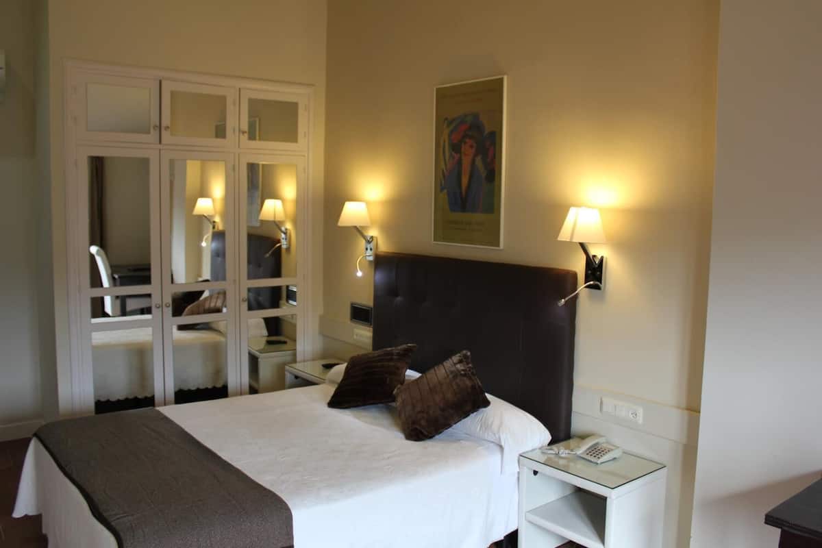Habitación de hotel con una cama grande, lámparas de noche, una mesita de noche con teléfono, un armario con puertas espejadas y un cuadro en la pared.