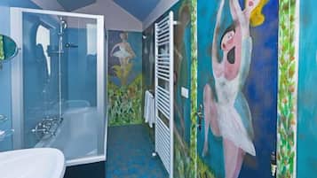 Casa de banho com chuveiro em cabine de vidro, lavatório branco e um mural na parede.
