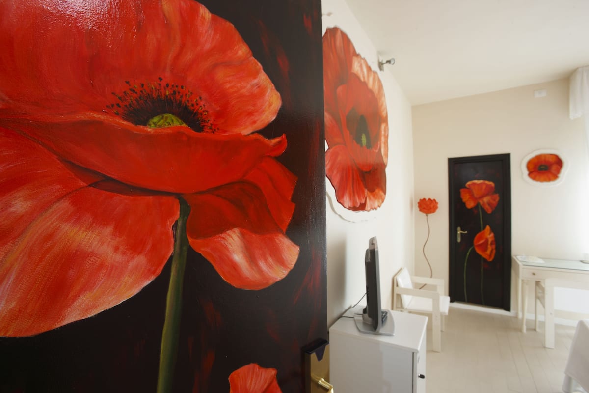 Ein Zimmer mit einem großen Gemälde von roten Mohnblumen an der Wand, einem weißen Schreibtisch und einem Stuhl.