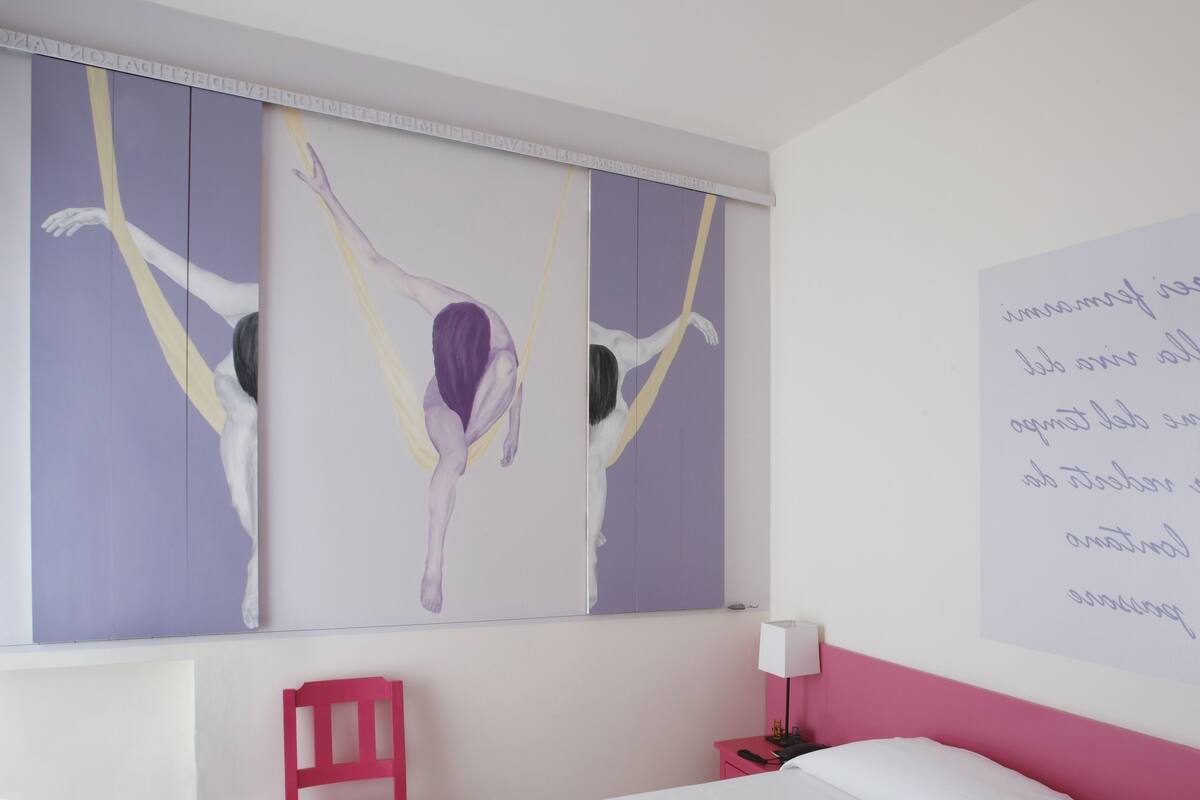 Ein Zimmer mit einem Bett, einem Nachttisch, einem roten Sessel und einer Wand mit einem Gemälde und einer handgeschriebenen Notiz.