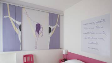 Une pièce comprenant un lit, une table de chevet, un fauteuil rouge et un mur orné d’un tableau et d’un mot écrit à la main.