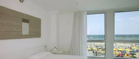 Habitación de hotel con un amplio ventanal que ofrece vistas a una playa concurrida.