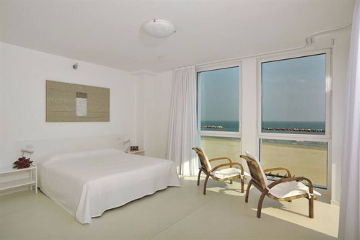 Ein Hotelzimmer mit einem großen Bett, zwei Sesseln am Fenster und Blick auf den Strand.