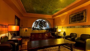 A warmly lit lounge area with leather seating, a wooden table, and a view of trees through an arched window. - Hotel Internacional (Porto)