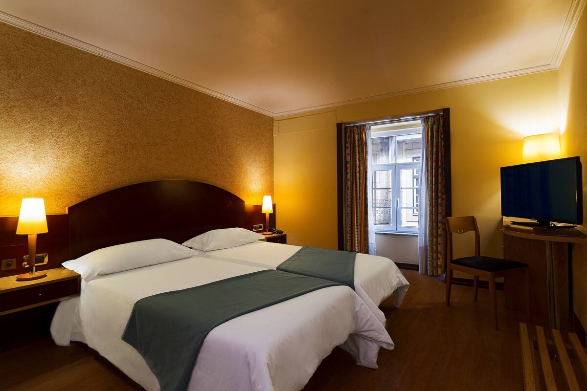 A hotel room with two beds, a television, a desk, and a chair.
