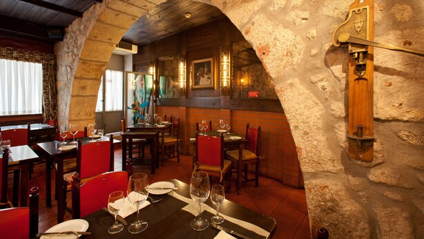 A restaurant with stone walls, wooden tables, and red chairs. - Hotel Internacional (Porto)