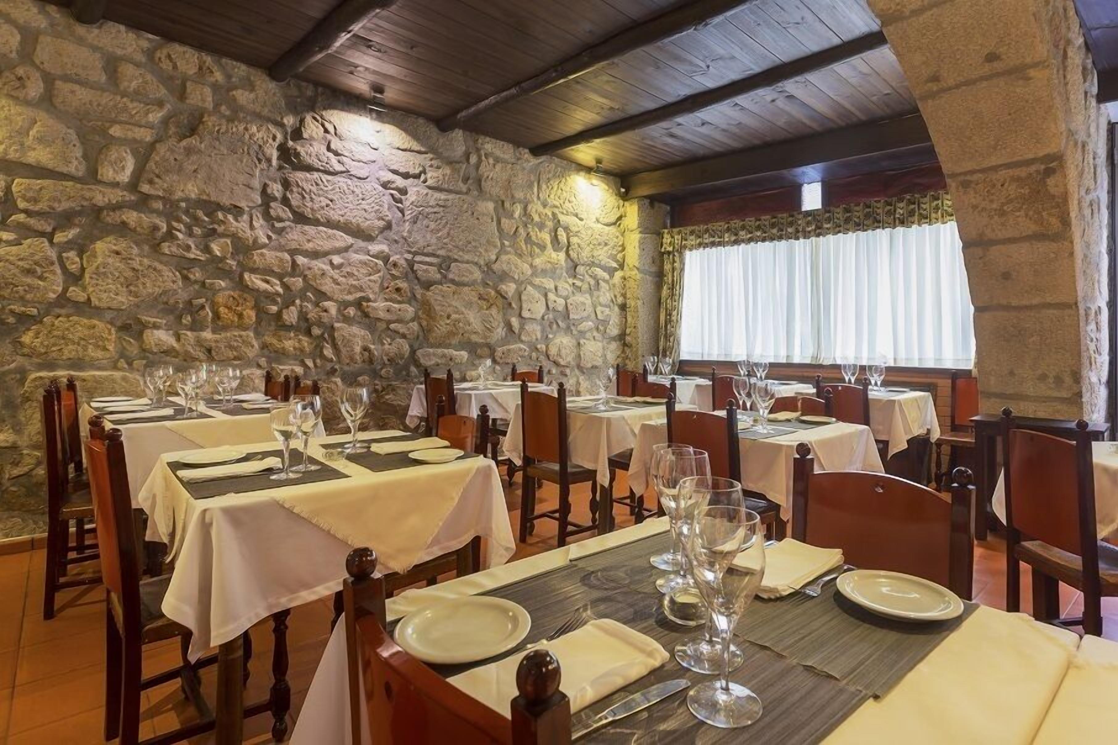 A restaurant with stone walls and wooden beams, tables set with white tablecloths and wine glasses.