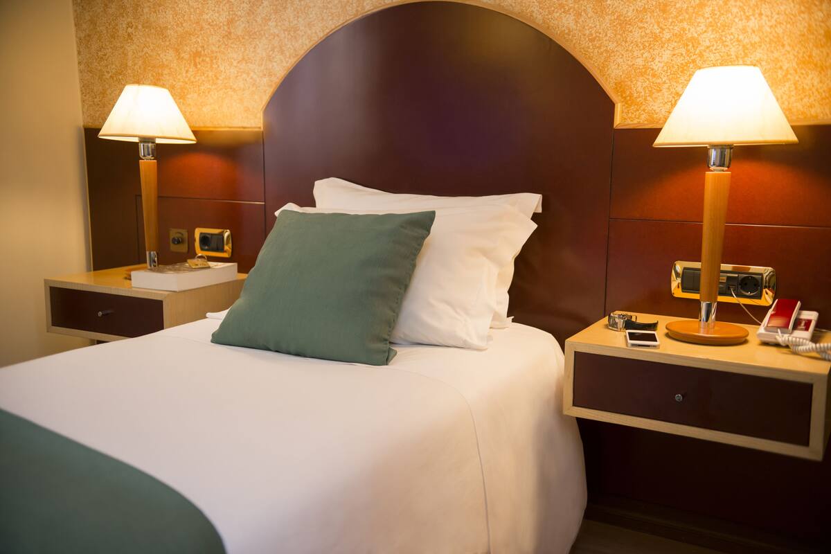 A hotel room with a large bed, two bedside tables, lamps, a phone, and a small clock.