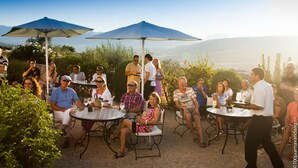 An outdoor patio with round tables and chairs, surrounded by greenery and a mountainous backdrop. - Arriadh Hotel (Ronda)