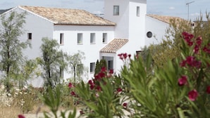 A white building with a tiled roof, surrounded by greenery and flowering plants. - Arriadh Hotel (Ronda)