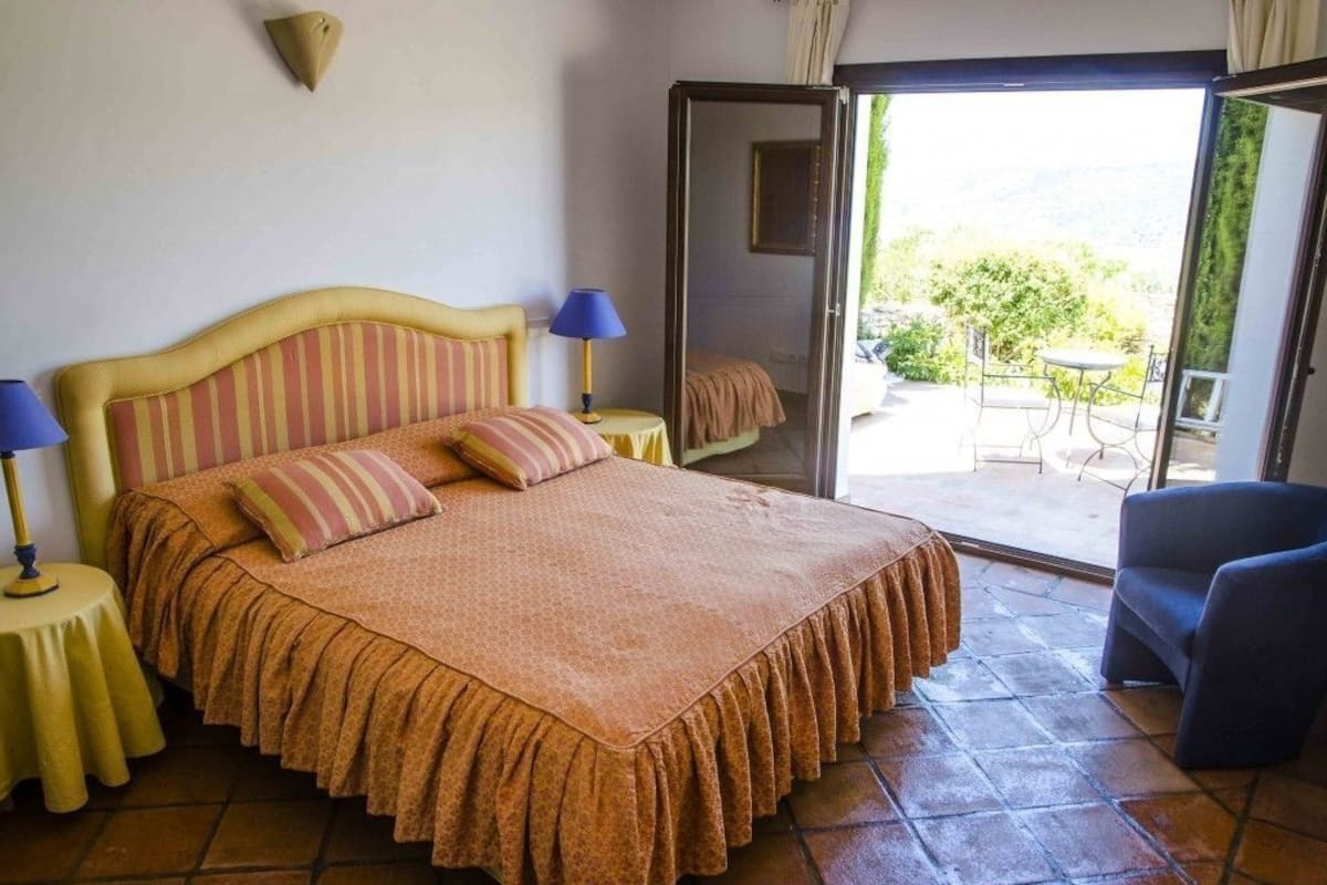Een slaapkamer met een bed, twee nachtkastjes met lampen, een schuifdeur naar een terras en een stoel.