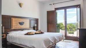 A bedroom with a large bed, a wooden headboard, a nightstand, and a view of the outdoors through a sliding glass door. - Arriadh Hotel (Ronda)
