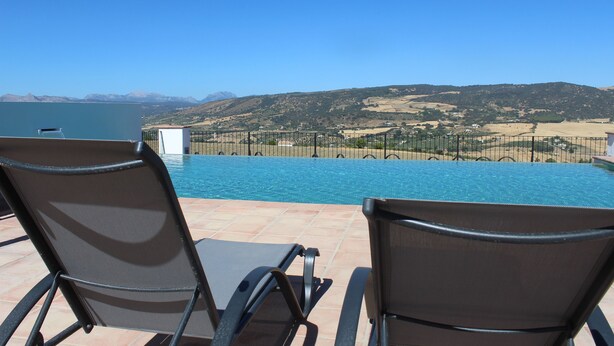 A poolside area with two lounge chairs facing a pool and a scenic view of hills and mountains. - Arriadh Hotel (Ronda)