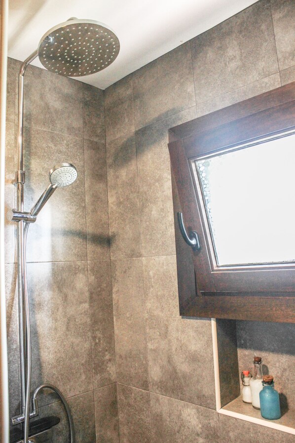 Ducha con cabezal de mano, puerta de vidrio y repisa con botellas.