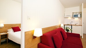 Ein Hotelzimmer mit Bett, einem roten Sofa, einer kleinen Küchenzeile mit Mikrowelle und einem Nachttisch mit Lampe.