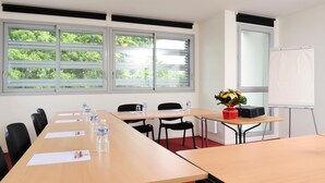 Ein Konferenzraum mit einem langen Tisch, Stühlen, einer Whiteboard und einem Fenster mit Blick auf Bäume.