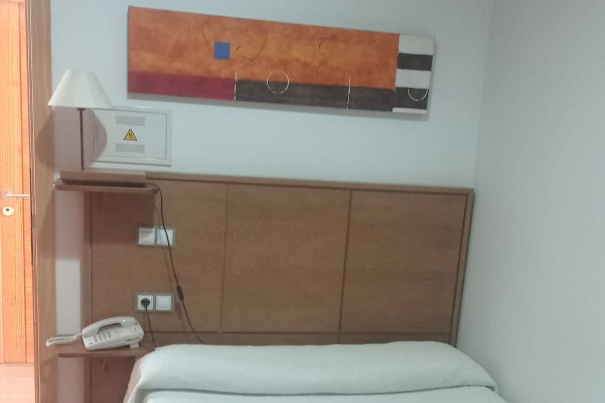 A room with a bed, a bedside table with a lamp, a phone, and a wall-mounted air conditioner.