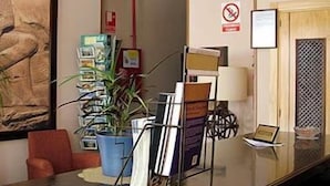 A reception area with a glass desk, a potted plant, a magazine rack, and a no-smoking sign.