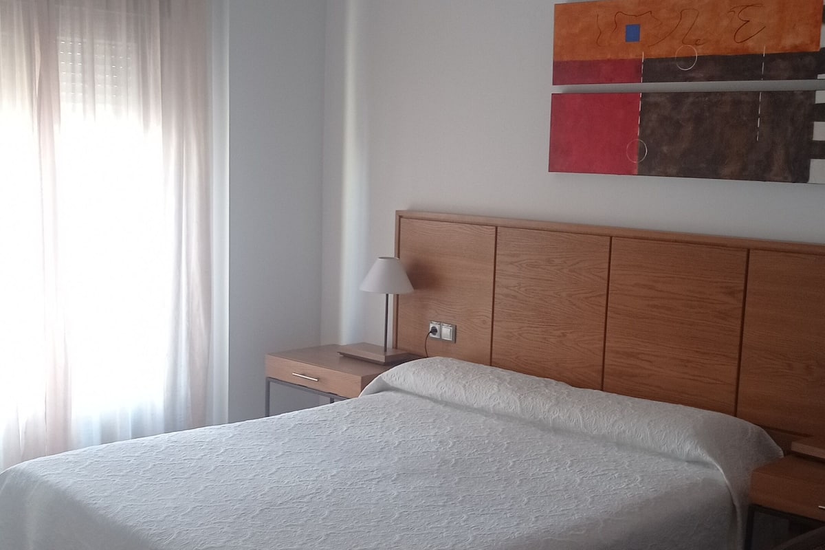 A bedroom with a large bed, a wooden headboard, a nightstand, a lamp, and a wall art piece.