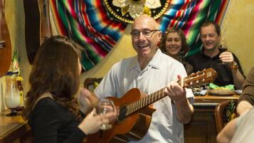 Un hombre tocando la guitarra en un bar, con una bandera colorida al fondo.