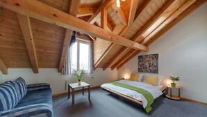 A bedroom with a loft-style ceiling, a bed, a sofa, a small table, and a potted plant. - Hotel Blume (Interlaken)