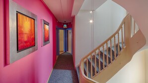 A hallway with pink walls, framed artwork, and a staircase with wooden railings. - Hotel Blume (Interlaken)
