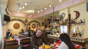A restaurant with round tables, colorful tablecloths, and a bar area with bottles and glasses. - Hotel Blume (Interlaken)